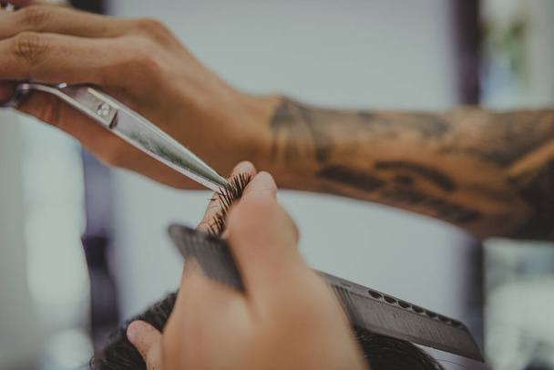 detal młodego mężczyzny z wytatuowanymi ramionami obcina facetowi włosy w salonie fryzjerskim - Zdjęcie, obraz