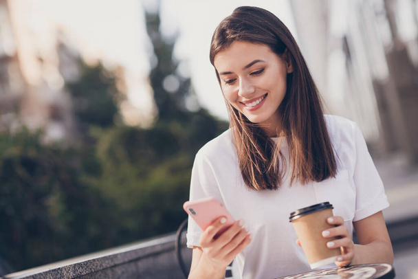 Photo portrait of girl holding phone paper cup smiling outdoors - Fotó, kép