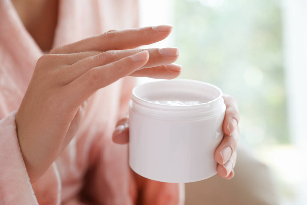 Woman with jar of moisturizing cream on blurred background, closeup - Fotoğraf, Görsel