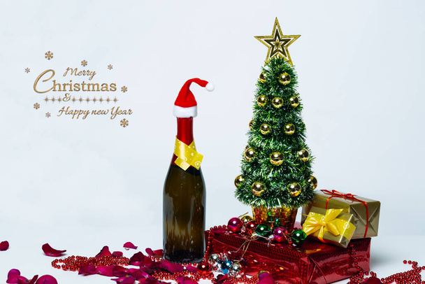 Kerstcompositie Champagne fles in kerstmuts en traditionele decoraties. Nieuwjaarskaart. Gedecoreerde kerstboom, kerstcadeaus met champagne op wit. - Foto, afbeelding
