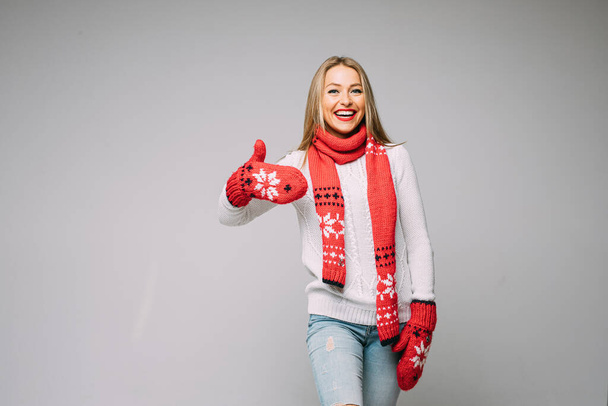 ελκυστική γυναίκα σε λευκό πουλόβερ, κόκκινο κασκόλ και κόκκινα γάντια με χριστουγεννιάτικα σχέδια δείχνει σαν - Φωτογραφία, εικόνα
