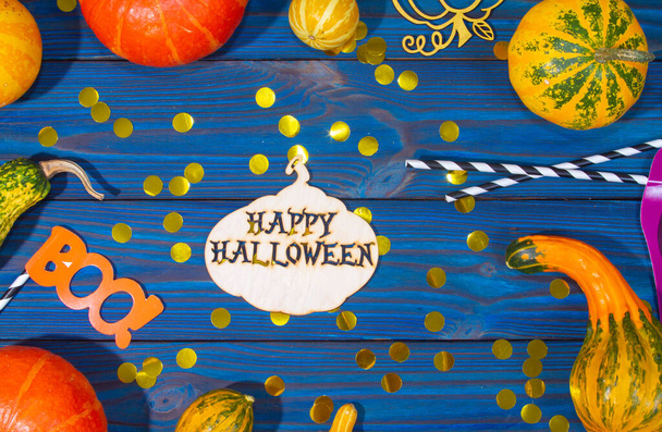 Verschiedene Kürbisse, dekoratives kleines gebogenes Gemüse auf blauem Holzgrund, die Inschrift "Happy Halloween", die Buchstaben "Boo", Goldfunkeln auf der Tafel. - Foto, Bild
