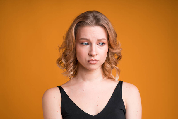 A portrait of a moody Caucasian girl isolated on orange background. She's dissapointed and sad, looking sideways and pouting lips - Φωτογραφία, εικόνα