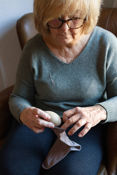 Стара жінка ремонтує шкарпетку вдома
 - Фото, зображення