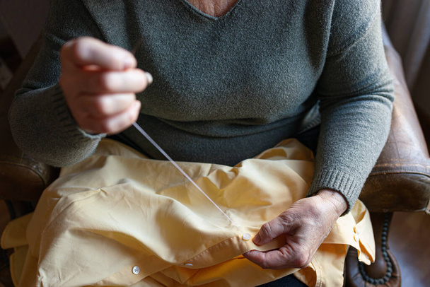 Стара жінка пришиває ґудзик вдома
 - Фото, зображення