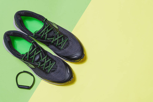 vista superior de un par de zapatos deportivos negros y verdes y una pulsera inteligente negra con un fondo verde y amarillo con espacio para copiar a la derecha - Foto, Imagen