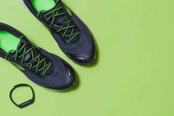 top view of a pair of black and green sport shoes and black smart wristband with a green background with copy space on the right - Photo, Image