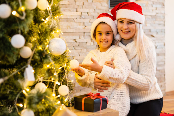 Счастливого Рождества и счастливых праздников. Мама и дочь украшают елку в комнате. Любить семью в помещении. - Фото, изображение