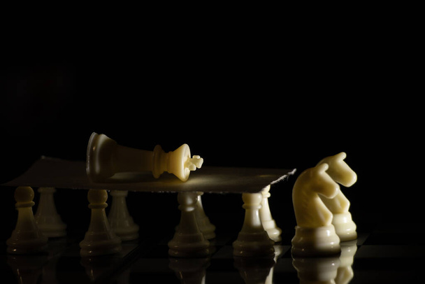 fehér sakkfigurák egy táblán fekete alapon, sakkozás - Fotó, kép