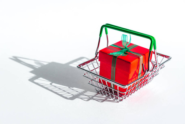 Grocery basket with red gift box on white isolated background. Christmas shopping online. Copy space. Holiday sales and discounts on new year and black Friday. Trading business. Space for text. - Fotografie, Obrázek