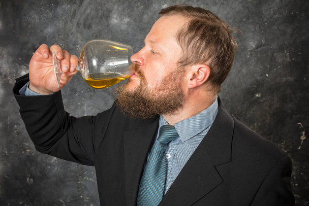 Solid bearded man in suit tasting whisky in a glass - Foto, Imagen