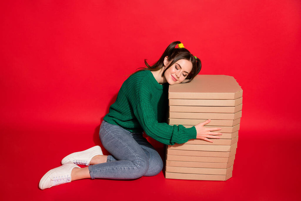 Hayalperest genç bayanın fotoğrafı yeşil örülmüş kazak giyer. Oturur, pizza kutularını kucaklar, izole edilmiş kırmızı arka plan. - Fotoğraf, Görsel