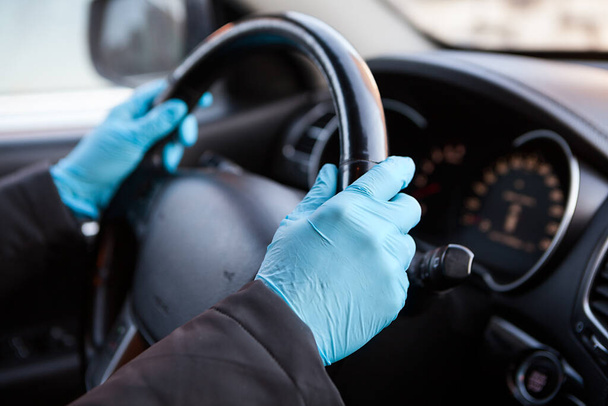 Drivers hands dressed in blue rubber gloves holding steering wheel of vehicle, close up view - Fotoğraf, Görsel