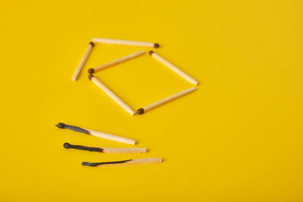 a silhouette of a house of matches and several burnt matches on a yellow background copy space - Foto, Bild
