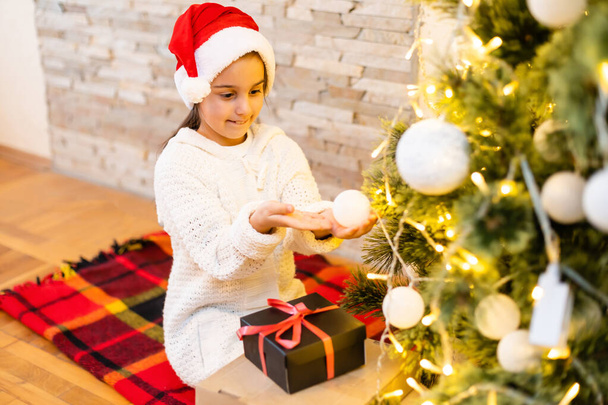 クリスマスツリーの上の部屋で笑って幸せな子供の女の子。スタイリッシュなセーターを着て。子供の頃。クリスマスタイム. - 写真・画像