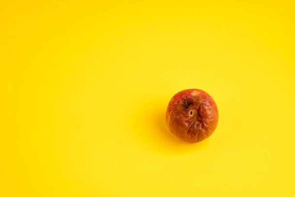 Rotten apple with a worm on a uniform yellow background. - Zdjęcie, obraz