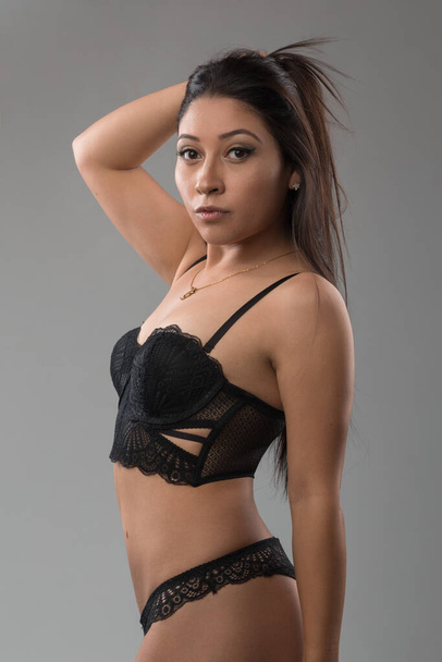 Latin slim woman holding her black hair, wears makeup and black lace lingerie, studio - Foto, afbeelding