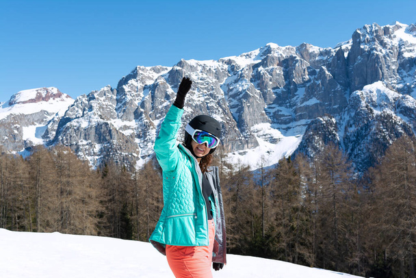 Eine Frau in buntem Skianzug, Helm und Sonnenbrille steht nach dem Skifahren vor der Kulisse der Berggipfel. Sportkonzept, Menschen, Reisen - Foto, Bild