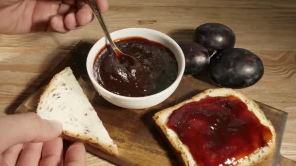 Uomo diffusione gustosa marmellata di prugne su pezzo di pane sul tavolo - Filmati, video