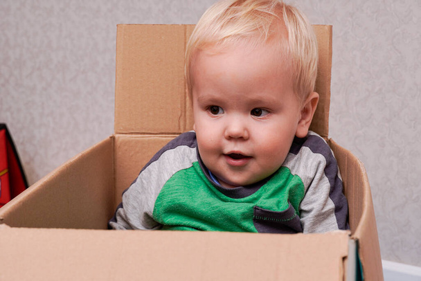 Little boy with blond hair sitting in a box. high quality - Фото, изображение