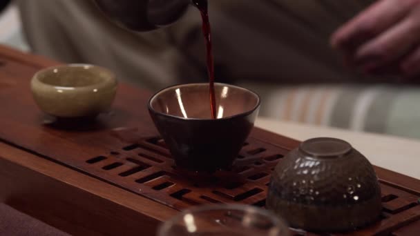 De verkoper en eigenaar van de theewinkel schenkt thee uit de theepot voor de klant en gast in keramische kommen om een proeverij theeceremonie uit te voeren. - Video
