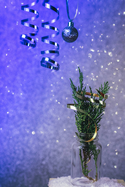 Ramitas de ciprés en un frasco de vidrio decorado con oropel sobre fondo azul brillante. Composición mínima de invierno. Concepto de Navidad o Año Nuevo, de cerca. - Foto, Imagen