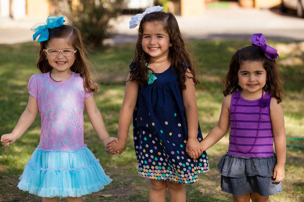 drei kleine Mädchen lächelnd und Händchenhaltend in einem Park an einem sonnigen Tag - Foto, Bild