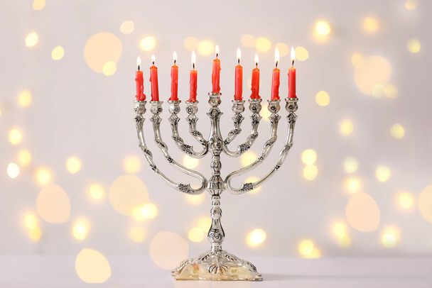Silver menorah with burning candles against light grey background and blurred festive lights. Hanukkah celebration - Fotoğraf, Görsel