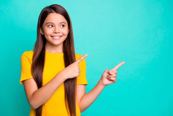 Positive kid girl point index finger empty space for promotion ads wear yellow clothes isolated on turquoise color background - 写真・画像