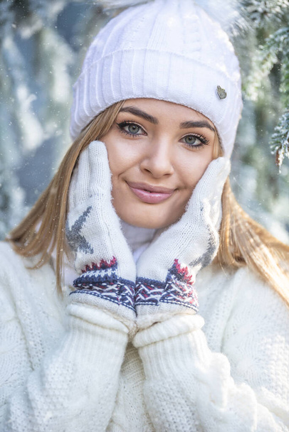 Gut aussehendes Mädchen berührt ihre weiche Gesichtshaut mit Winterhandschuhen, bekleidet mit einem Pullover und einer Mütze. - Foto, Bild