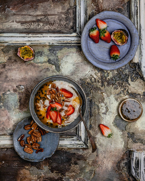 bowl with porridge and strawberries with passion fruit sauce and nuts on rustic table, close view healthy breakfast  - Zdjęcie, obraz