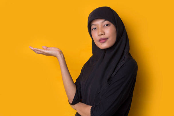 Jeune femme d'affaires asiatique portant hijab sur fond jaune souriant confiant pointant avec les doigts vers différentes directions. Espace de copie pour la publicité - Photo, image