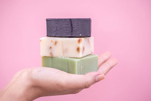 Refreshing soaps handmade of roses, aloe vera and active carbon held in one hand with a pink background and in close up concept. - Foto, Bild