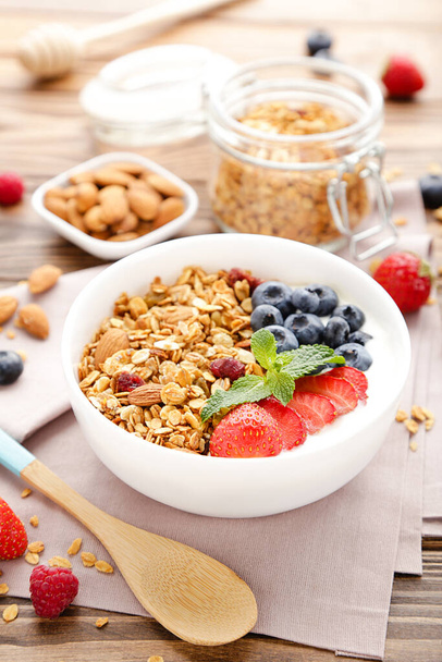 Tasty granola with fresh berries and spoon on brown wooden background - Фото, изображение