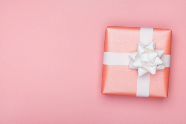 Cadeaudoosje met witte strik op roze ondergrond. Valentijnsdag, verjaardag of jubileum wenskaart. Bovenaanzicht, flat lay, kopieerruimte - Foto, afbeelding