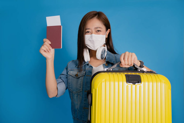 Turista asiática que lleva una máscara antivirus lleva una maleta y pasaportes con un billete de avión. Ella ha disfrutado el viaje. - Foto, imagen
