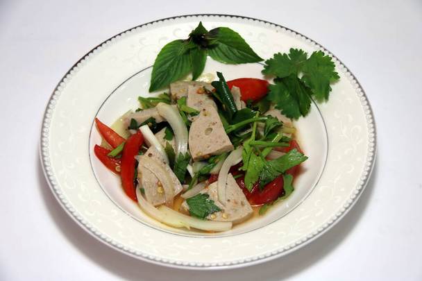 Ensalada de carne de cerdo vietnamita picante en la paleta blanca sobre el fondo blanco. Es comida picante del sudeste asiático, con un sabor amargo. - Foto, Imagen