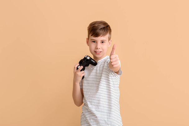 Cute boy with game pad showing thumb-up on color background - Photo, Image