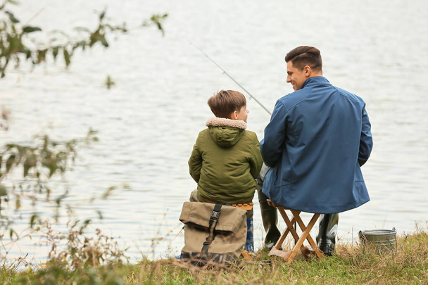 Το αγοράκι και ο πατέρας του ψαρεύουν στο ποτάμι. - Φωτογραφία, εικόνα