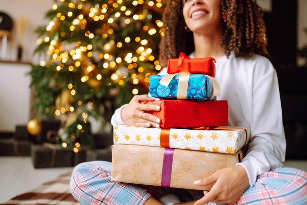 Christmas or New Year gift box in the female hands.  Happy woman opens presents near the Christmas tree. Winter holidays. - Foto, Imagem