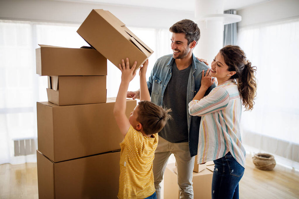 Happy young family with cardboard boxes in new house at moving day. - Photo, image