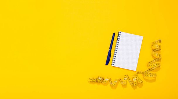 Twisted centimeter tape and spiral note book and pen with copy space on yellow background. Greeting postcard. Body measurement. Nutrition and fitness workout plan. International Women Day 8 March. - Фото, зображення