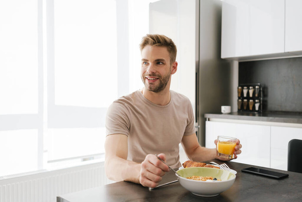 Young handsome caucasian man smiling while having breakfast at home - Foto, Imagen