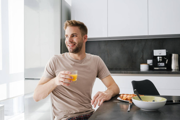 Young handsome caucasian man smiling while having breakfast at home - Photo, image