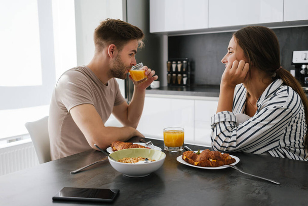 Young beautiful caucasian couple sitting at table while having breakfast at home - Foto, imagen
