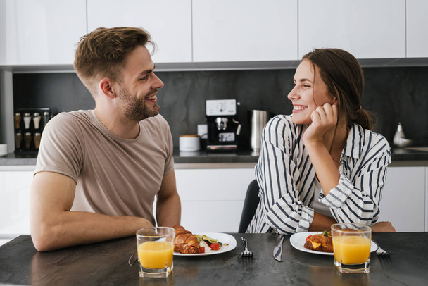 Young beautiful caucasian couple sitting at table while having breakfast at home - Photo, image