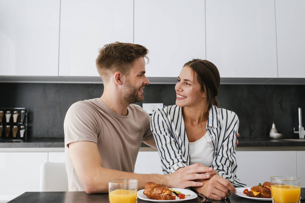 Young beautiful caucasian couple sitting at table while having breakfast at home - Photo, image