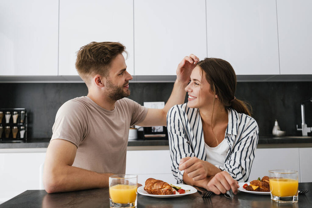 Young beautiful caucasian couple sitting at table while having breakfast at home - Photo, Image