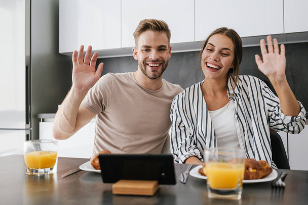 Young caucasian couple waving at cellphone while having breakfast at home - Zdjęcie, obraz