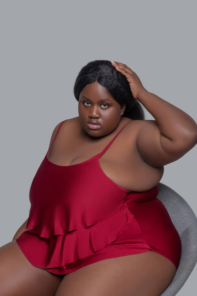 Plus size african american young woman in red underwear sitting on a chair - Fotó, kép